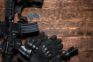 Special agent concept. Airsoft rifle and gloves on brown wooden table background with copy space.